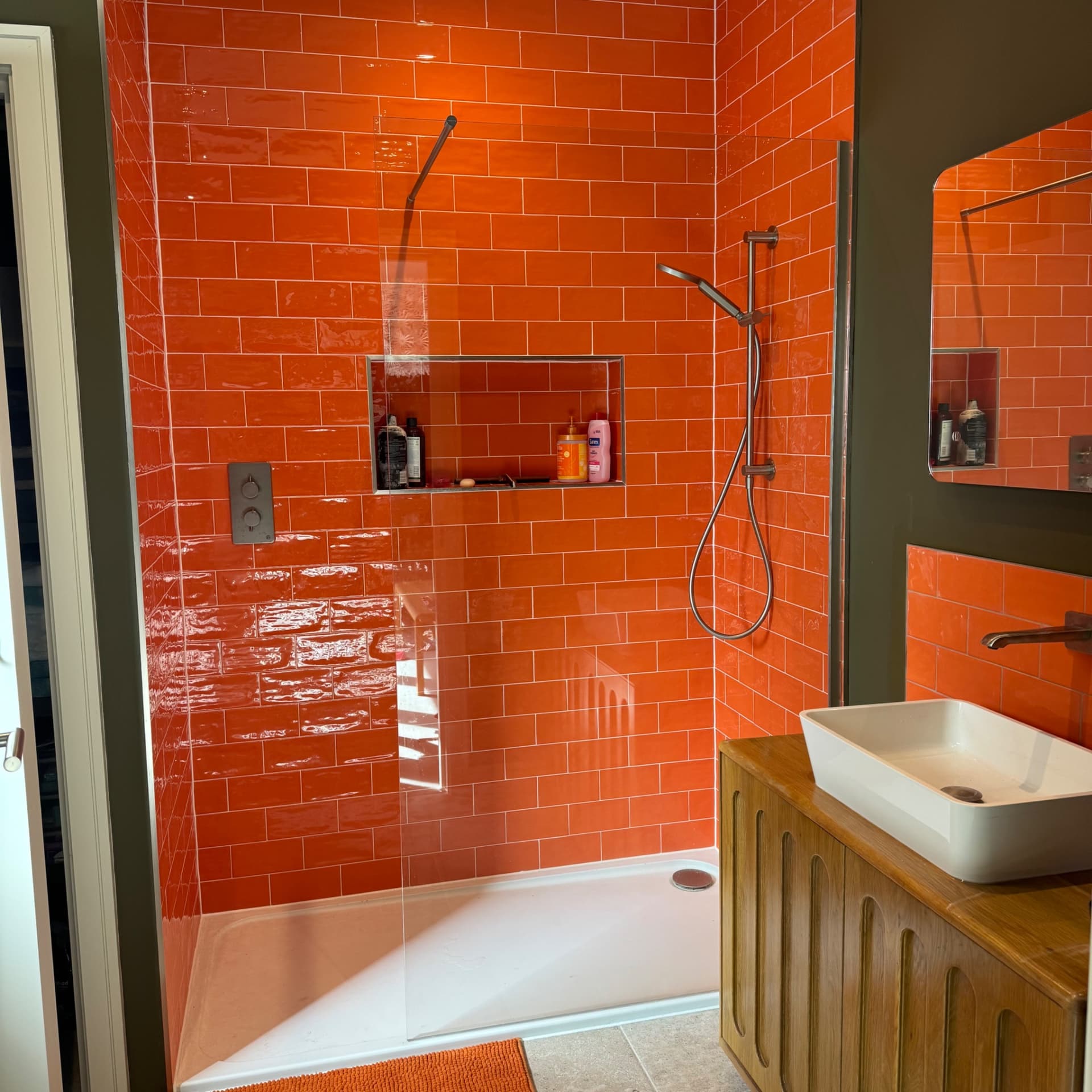 We've finished tiling this bathroom with vibrant orange metro tiles throughout the shower and splash back around the sink. We built in a recessed shelf in the shower for storing bottles, and chose matt brass trim to keep things subtle and let the tiles do the talking. It's a bold look that really works.