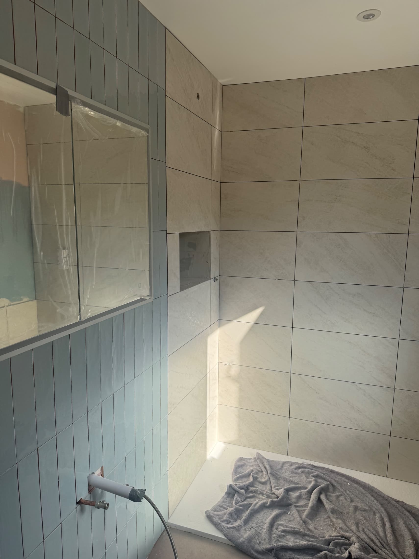 We're making good progress on day one — half the walls are now tiled, including the feature wall with the vertical tiles. Tomorrow we'll finish laying the remaining tiles ready for grouting.