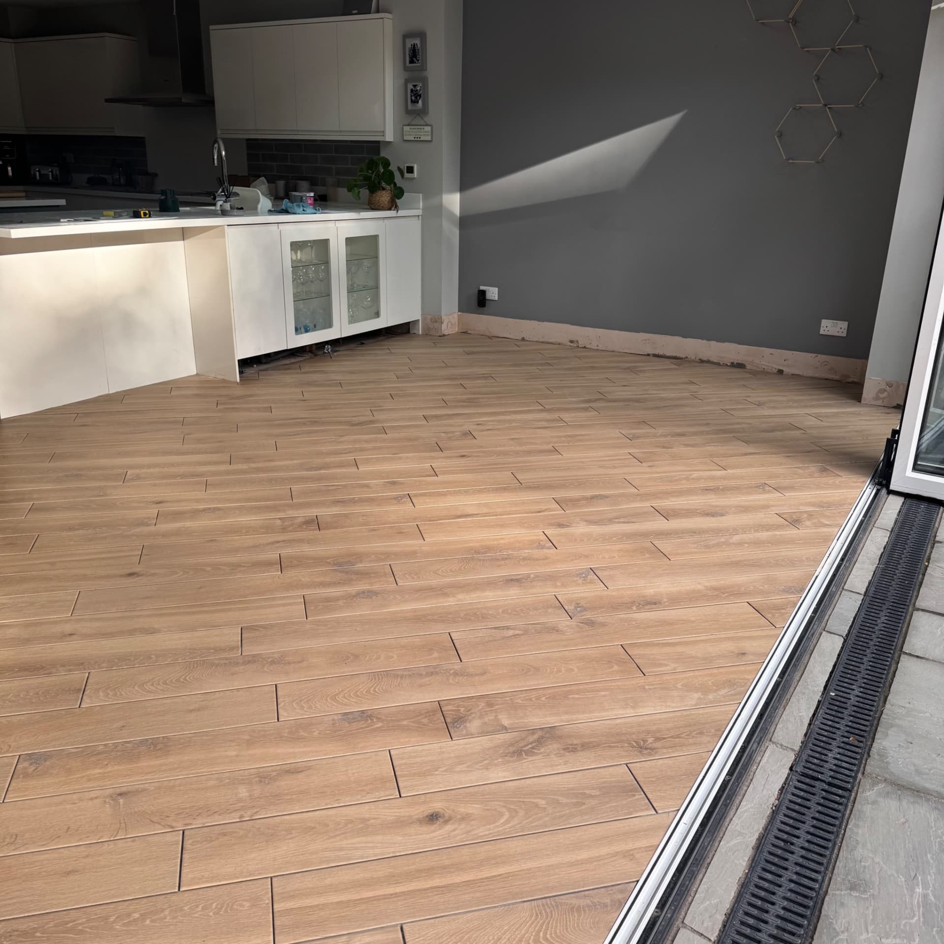 We've tiled right up to the bifold doors with a neat finish using edging trim, and we've adapted the layout to work around a height difference from when the doors were originally fitted. The result is a seamless look that works perfectly with the new kitchen space. Next step is the grouting.